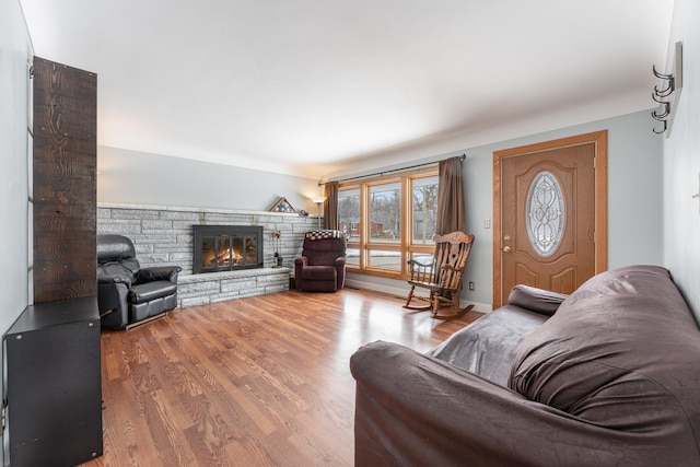 living room with a stone fireplace, baseboards, and wood finished floors