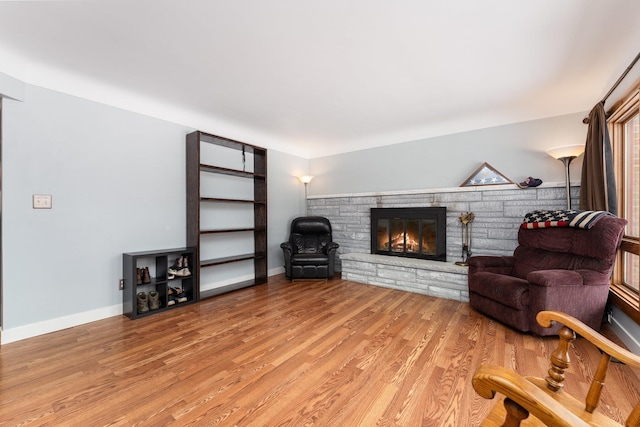 living area featuring a stone fireplace, light wood finished floors, and baseboards