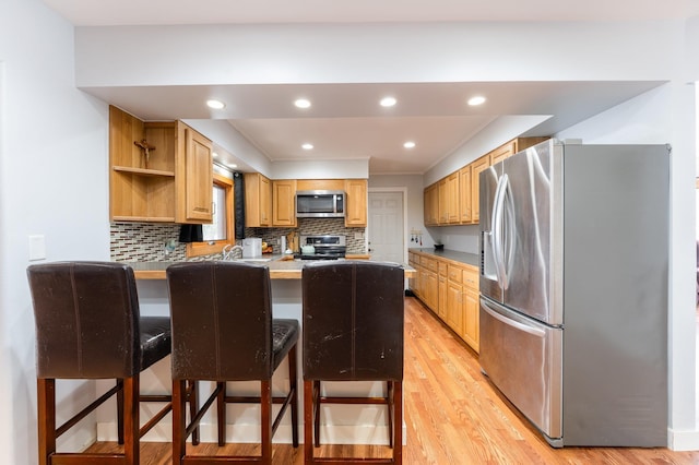 kitchen with appliances with stainless steel finishes, light wood-style floors, a peninsula, and decorative backsplash