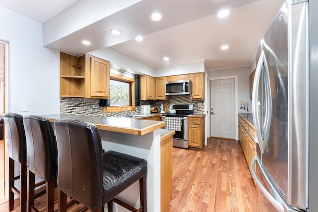 kitchen featuring light wood finished floors, appliances with stainless steel finishes, a breakfast bar area, a peninsula, and open shelves