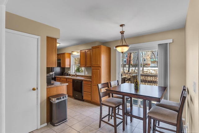 kitchen featuring light tile patterned floors, black dishwasher, brown cabinets, light countertops, and pendant lighting