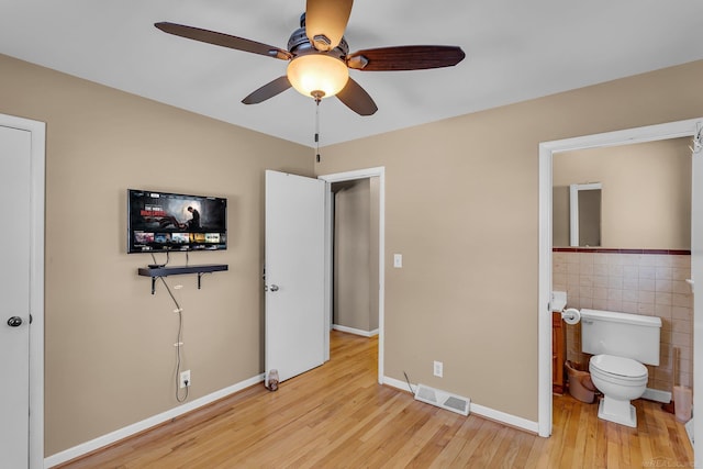 bedroom with baseboards, visible vents, ensuite bathroom, light wood-style floors, and tile walls