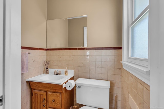 bathroom featuring toilet, wainscoting, tile walls, and vanity