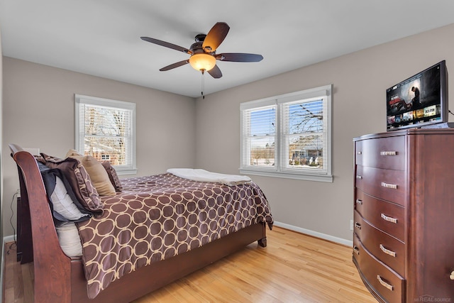 bedroom featuring light wood-type flooring, multiple windows, baseboards, and a ceiling fan