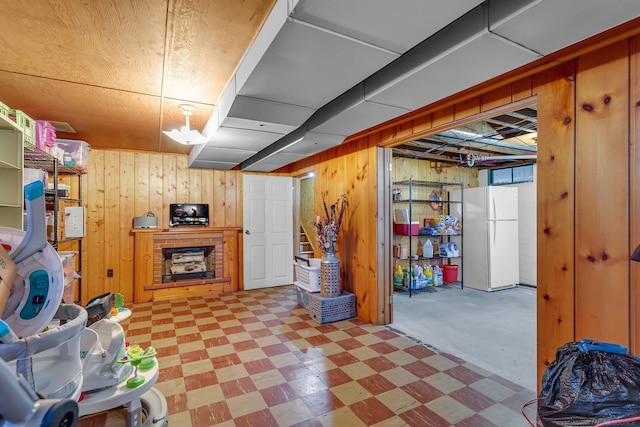 finished below grade area with a fireplace, tile patterned floors, freestanding refrigerator, and wooden walls