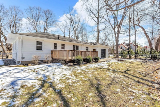 snow covered back of property with a garage, fence, and a deck