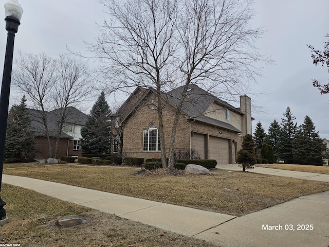 view of side of home featuring concrete driveway, brick siding, and a chimney