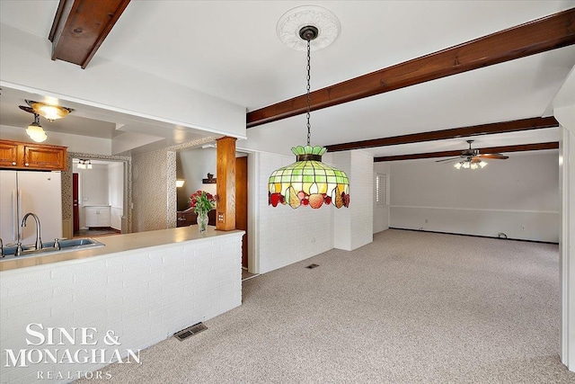 kitchen with visible vents, brown cabinetry, freestanding refrigerator, a sink, and beam ceiling