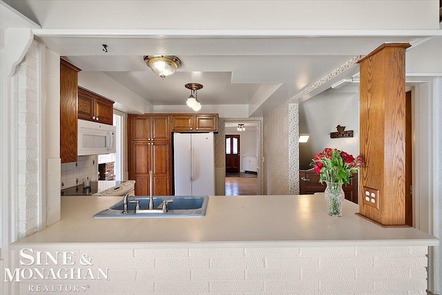 kitchen featuring light countertops, white appliances, brown cabinets, and a peninsula