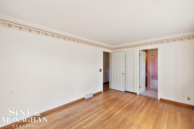 unfurnished bedroom with light wood finished floors, visible vents, baseboards, and ensuite bathroom