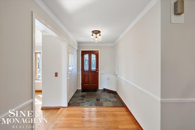 foyer entrance featuring dark wood-type flooring, a chandelier, ornamental molding, and baseboards