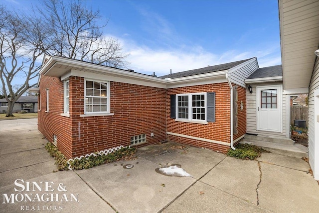 view of property exterior with brick siding, a patio, and driveway