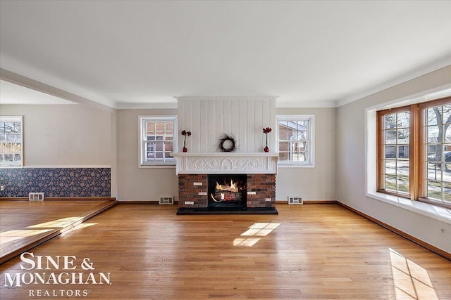 unfurnished living room with baseboards, a fireplace, visible vents, and wood finished floors