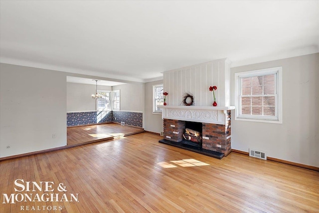 living area featuring a chandelier, a fireplace, wood finished floors, visible vents, and baseboards