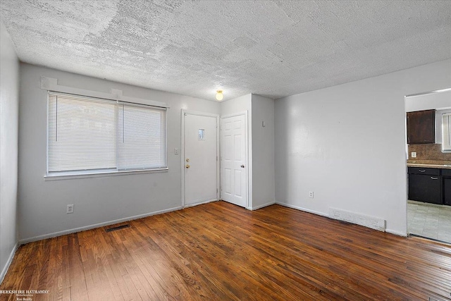 spare room with wood-type flooring, visible vents, and baseboards