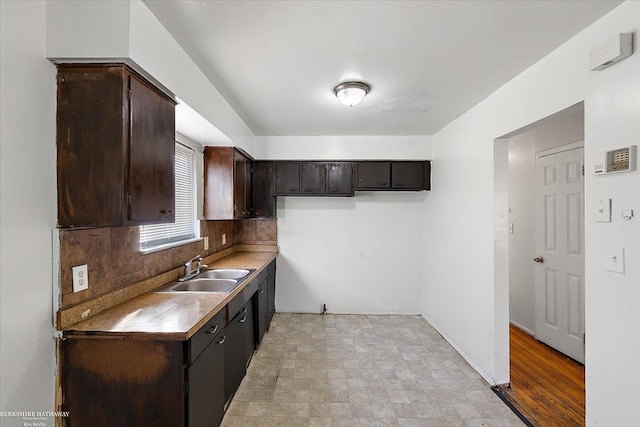 kitchen featuring dark brown cabinetry, backsplash, a sink, and light floors