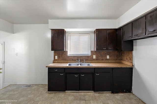 kitchen featuring a sink, visible vents, light countertops, dark brown cabinets, and decorative backsplash