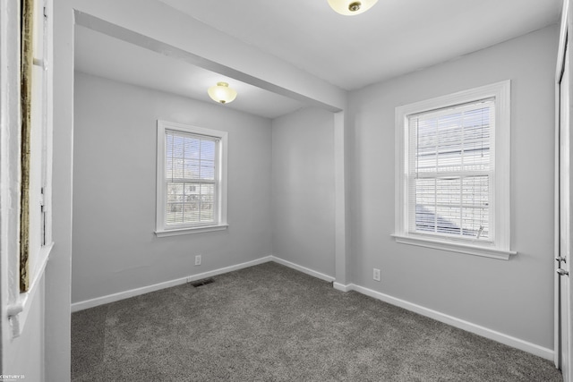 spare room with dark carpet, visible vents, and baseboards