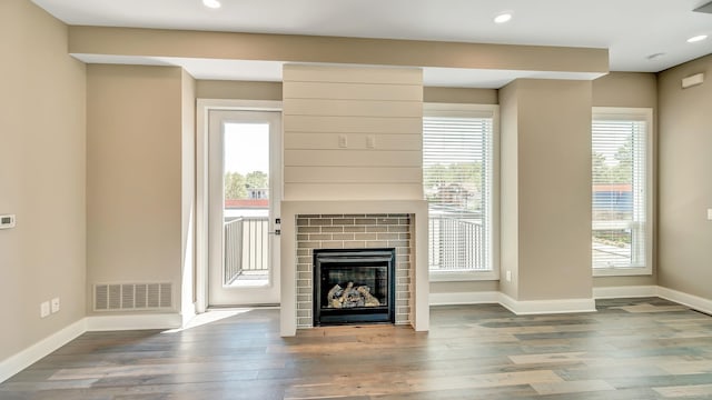 unfurnished living room featuring a glass covered fireplace, visible vents, plenty of natural light, and wood finished floors