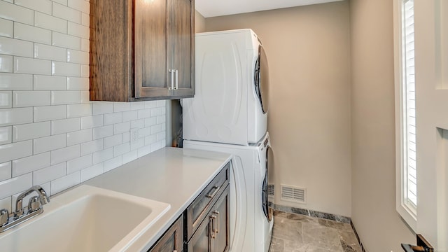 laundry room with a sink, visible vents, cabinet space, stone finish floor, and stacked washer and clothes dryer