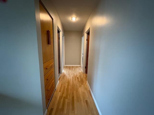 hallway featuring light wood finished floors and baseboards