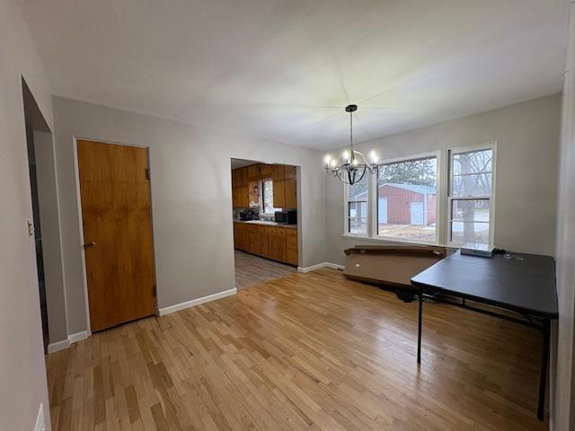 unfurnished dining area with baseboards, light wood-type flooring, and a notable chandelier