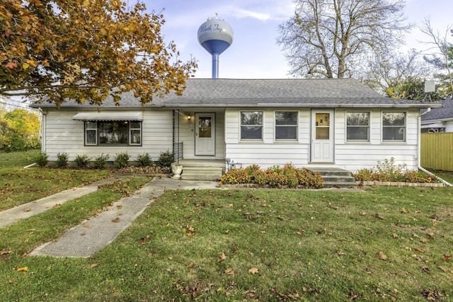 ranch-style home with a shingled roof, fence, and a front yard