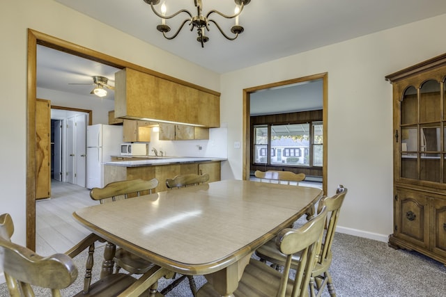 dining area with light carpet, ceiling fan with notable chandelier, and baseboards