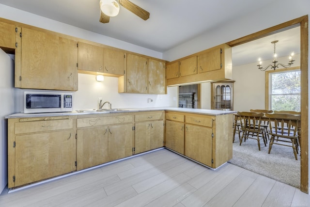 kitchen featuring white microwave, light countertops, a sink, and ceiling fan with notable chandelier