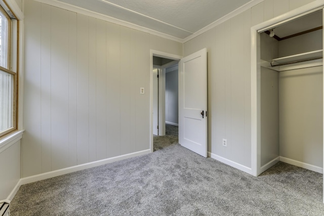 unfurnished bedroom featuring a baseboard heating unit, multiple windows, carpet, and crown molding