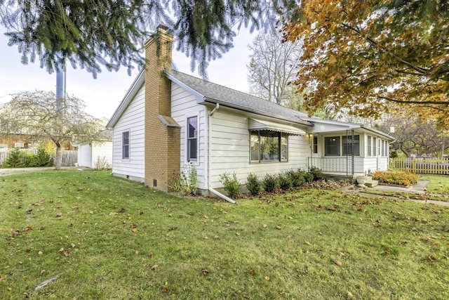 view of home's exterior featuring fence, a sunroom, a yard, roof with shingles, and a chimney