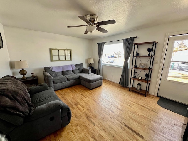 living room featuring light wood-style floors, ceiling fan, baseboards, and a textured ceiling