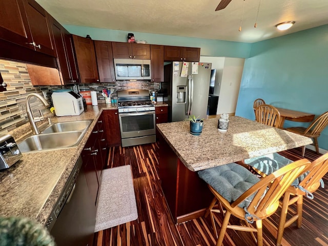 kitchen with dark wood finished floors, ceiling fan, a center island, stainless steel appliances, and a sink