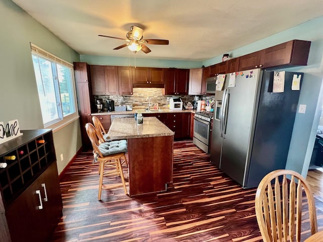 kitchen with dark wood-style flooring, a sink, a center island, appliances with stainless steel finishes, and decorative backsplash