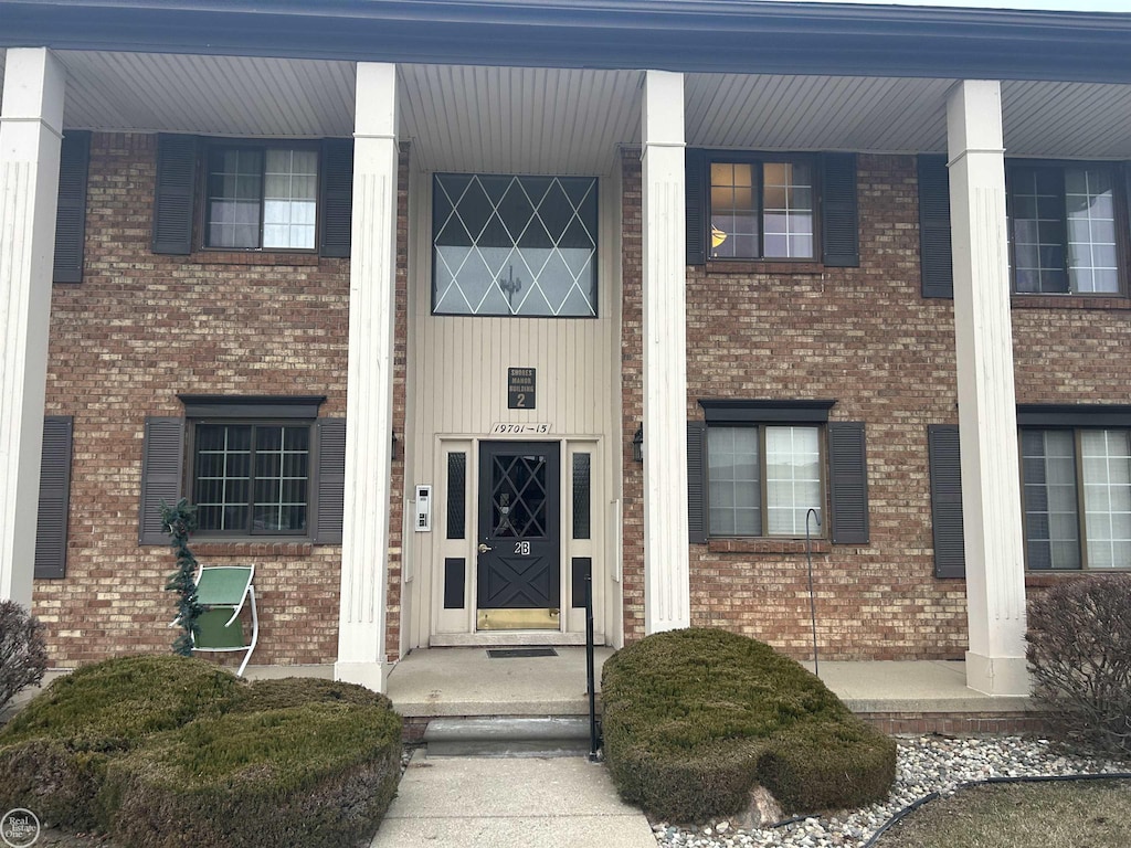 view of exterior entry featuring covered porch and brick siding