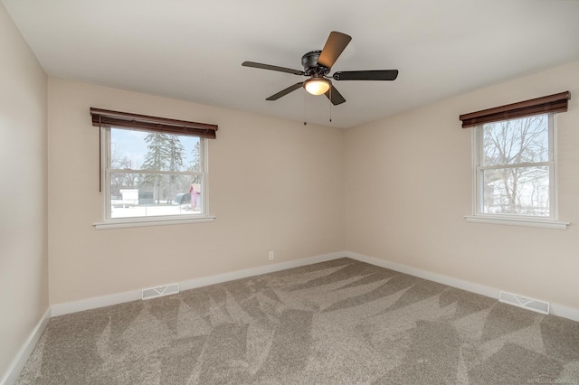 carpeted spare room featuring plenty of natural light, visible vents, and baseboards