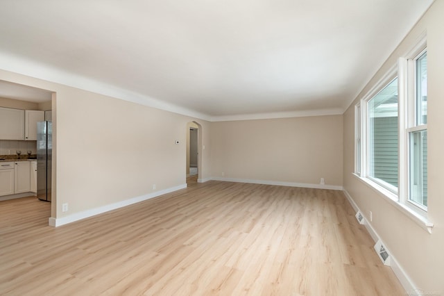 unfurnished room with arched walkways, light wood finished floors, visible vents, and baseboards