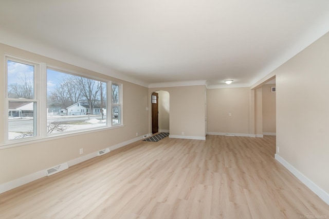 spare room with arched walkways, light wood finished floors, visible vents, and baseboards