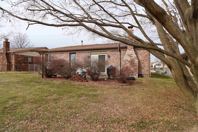 rear view of house featuring a yard, a chimney, fence, and brick siding