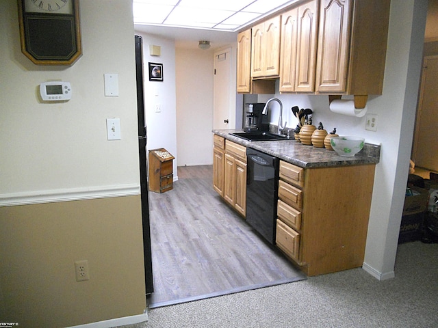 kitchen featuring black dishwasher, dark countertops, light colored carpet, a sink, and baseboards