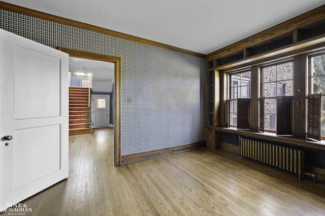 empty room with radiator, a healthy amount of sunlight, stairs, and hardwood / wood-style floors