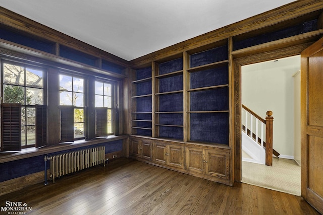 empty room with dark wood-style floors, radiator, stairway, and built in shelves