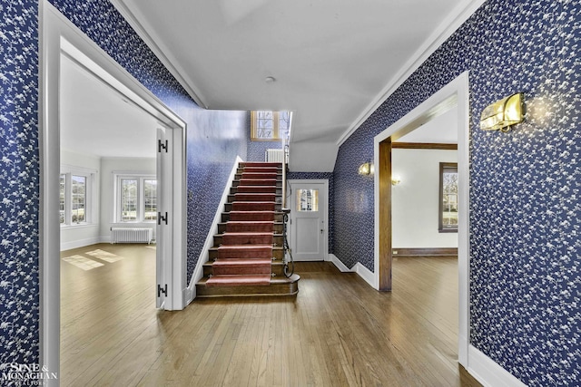 entrance foyer featuring wallpapered walls, radiator heating unit, wood-type flooring, stairway, and ornamental molding