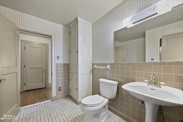 bathroom featuring tile patterned flooring, a wainscoted wall, toilet, and wallpapered walls