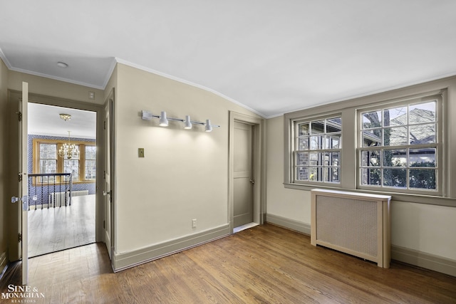 unfurnished room featuring radiator heating unit, crown molding, baseboards, and wood finished floors