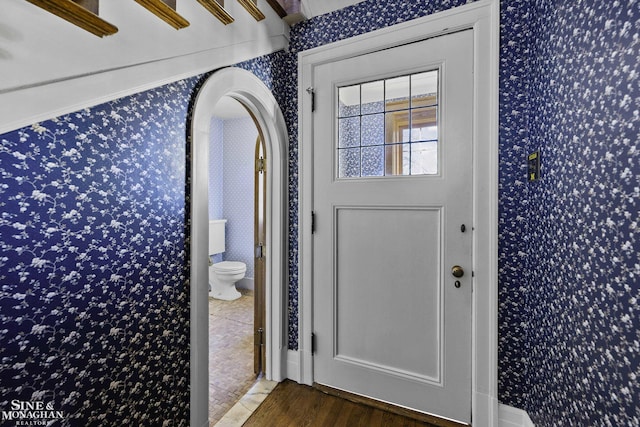 foyer entrance with wallpapered walls, arched walkways, and wood finished floors