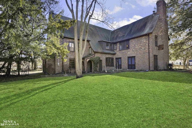 rear view of property featuring a chimney, a lawn, and brick siding