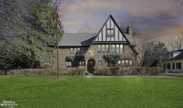 tudor-style house with stone siding, a chimney, and a front lawn