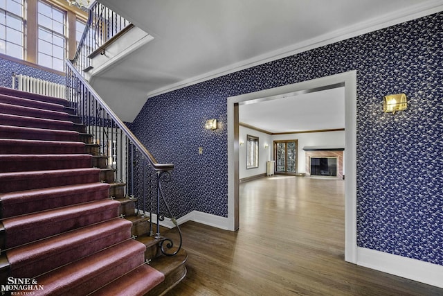 stairs featuring wood finished floors, baseboards, wallpapered walls, a glass covered fireplace, and crown molding