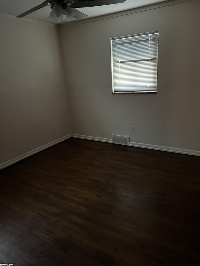 empty room with dark wood finished floors, crown molding, visible vents, a ceiling fan, and baseboards